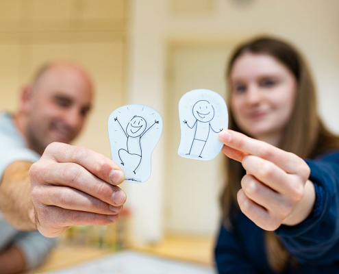 Ein Mann und eine Frau halten auf Papier gezeichnete Strichmännchen hoch