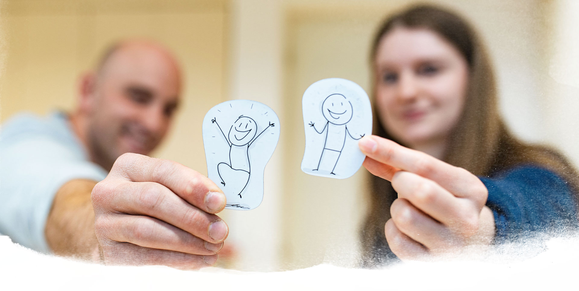 Ein Mann und eine Frau halten auf Papier gezeichnete Strichmännchen hoch