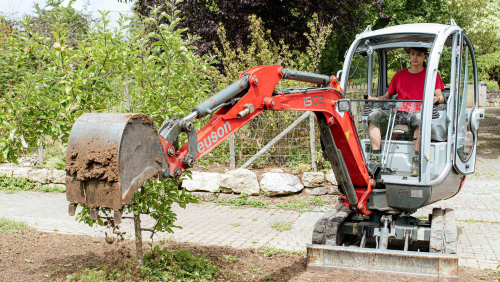 Auszubildender im Gartenbau schaufelt Erde mit kleinem Bagger.