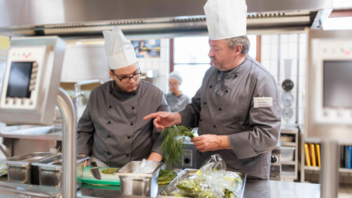 Auszubildende in der Großküche mit Ausbilder beim Kochen