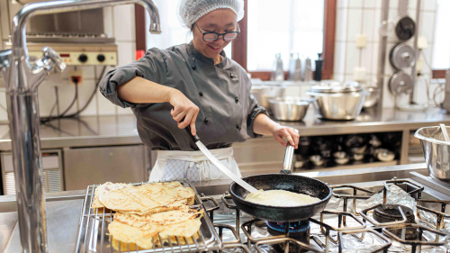 Auszubildende in der Großküche beim Backen von Pfannkuchen.