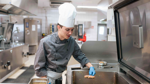 Auszubildender in der Großküche beim Braten von Fleischküchle.
