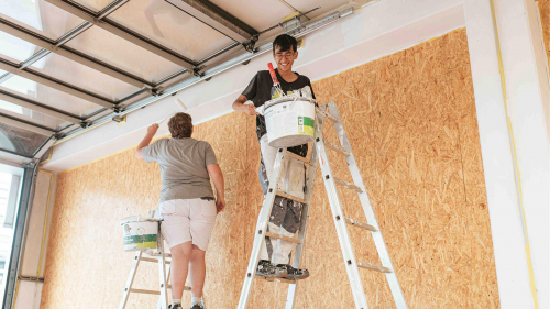 Auszubildende stehen auf der Leiter und streichen die Wand.