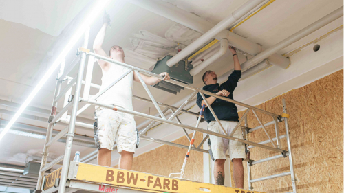 Auszubildende stehen auf einem Gerüst und streichen die Decke.