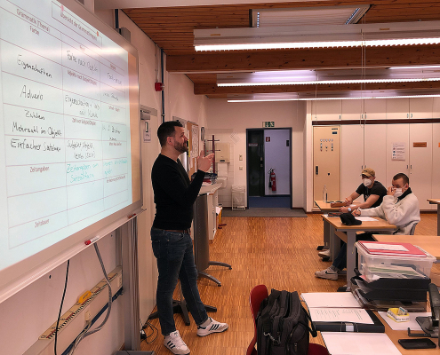 Gebärdensprachdozent steht am Whiteboard vor Schüler*innen