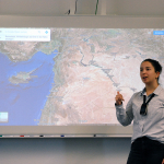 Lehrerin steht mit Mikrofon vor Whiteboard
