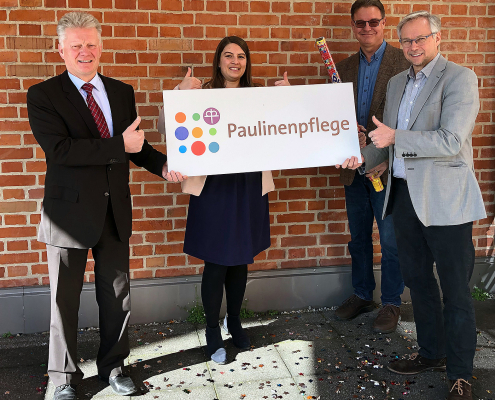 Drei Männer und eine Frau halten ein Schild mit dem neuen Logo der Paulinenpflege