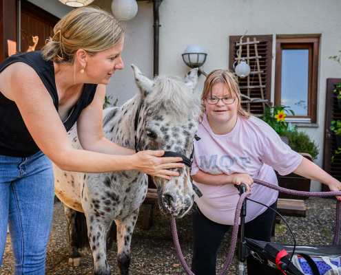 Tierpädagogin und betreute Frau stehen neben einem Pony