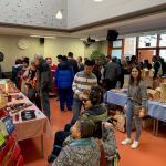 Weihnachtsmarkt-Besucher scharen sich um Tische mit verschiedenen Verkaufs-Produkten.