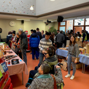 Weihnachtsmarkt-Besucher scharen sich um Tische mit verschiedenen Verkaufs-Produkten.