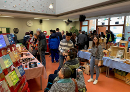 Weihnachtsmarkt-Besucher scharen sich um Tische mit verschiedenen Verkaufs-Produkten.