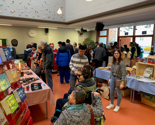 Weihnachtsmarkt-Besucher scharen sich um Tische mit verschiedenen Verkaufs-Produkten.