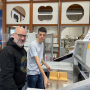 Ein älterer und jüngerer Mann stehen an einer großen Schneidemaschine.