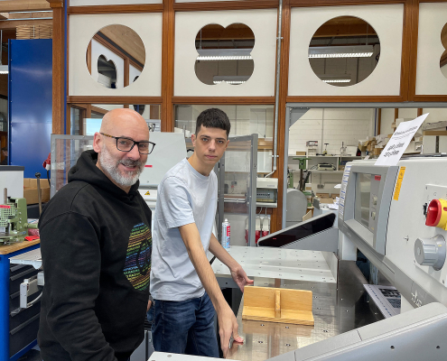 Ein älterer und jüngerer Mann stehen an einer großen Schneidemaschine.