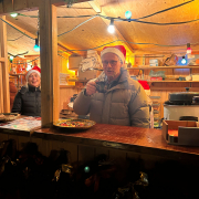 Ein Mann und eine Frau mit Weihnachtsmann-Mütze schauen aus dem Verkaufsstand heraus.