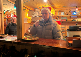 Ein Mann und eine Frau mit Weihnachtsmann-Mütze schauen aus dem Verkaufsstand heraus.