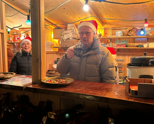 Ein Mann und eine Frau mit Weihnachtsmann-Mütze schauen aus dem Verkaufsstand heraus.