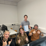 Ein Lehrer, zwei Schülerinnen und ein Schüler zeigen stolz eine Urkunde.