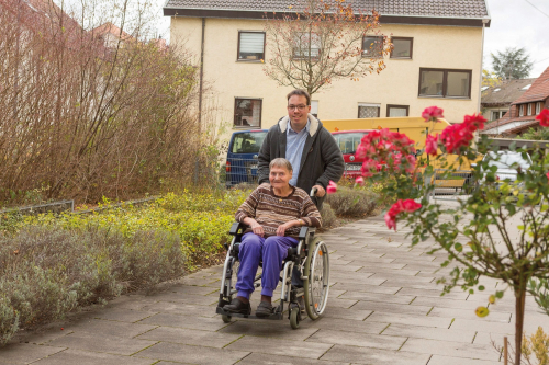 Junger Mann schiebt den Rollstuhl einer älteren Frau beim Spazieren gehen