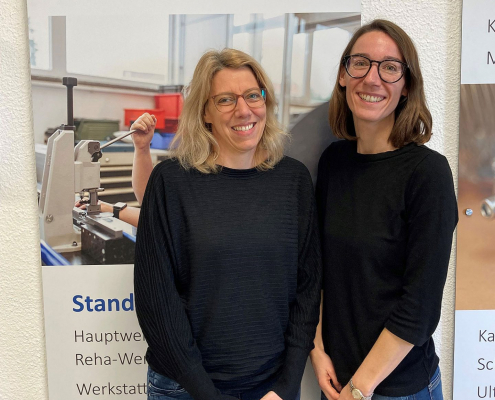 Zwei Frauen stehen vor einem Plakat der Backnanger Werkstätten.