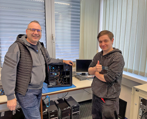 IT-Asubilder und IT-Azubi stehen vor offenem Desktop-PC