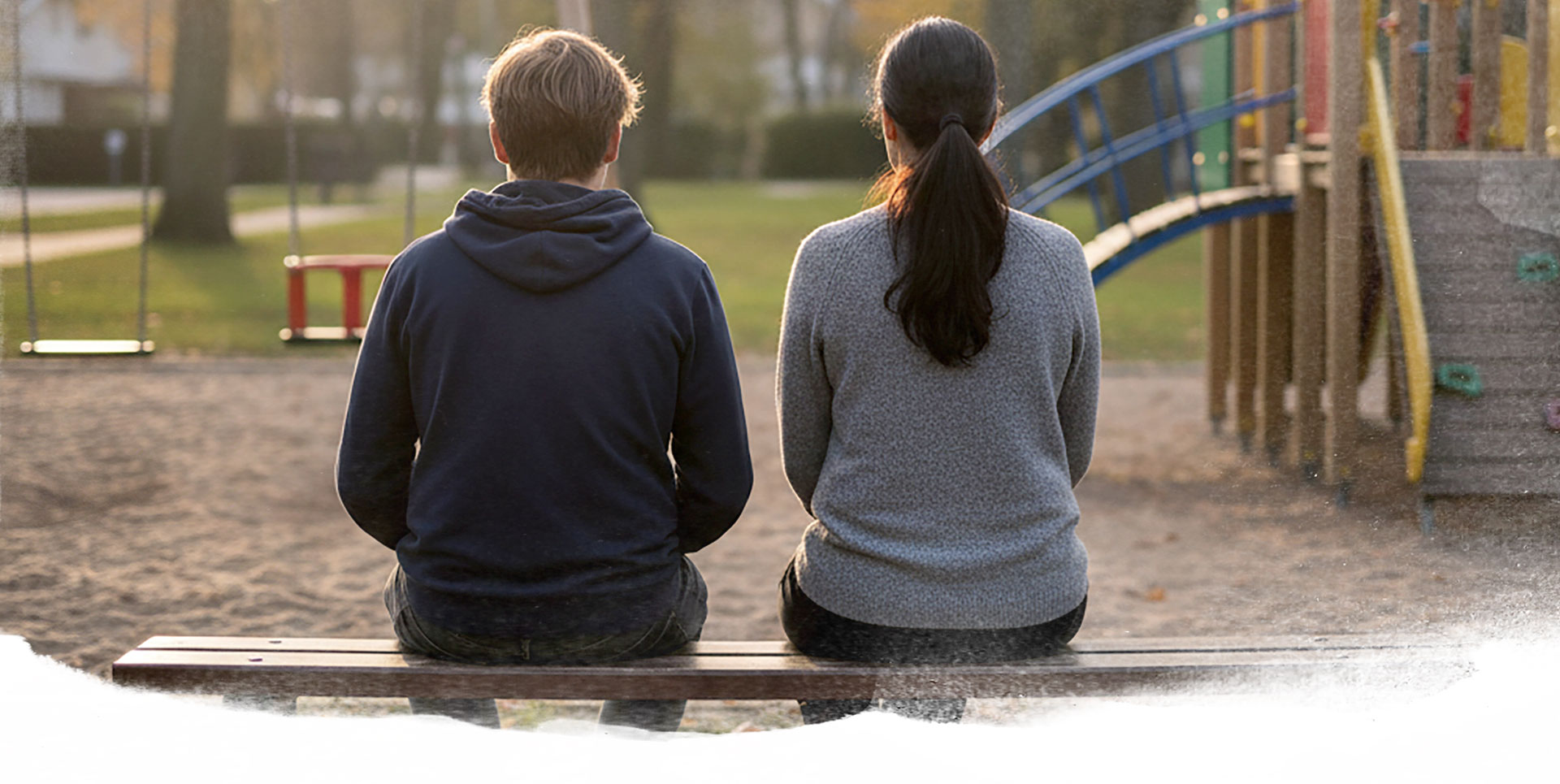 Junges Paar sitzt auf einer Bank am Spielplatz