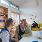 Eine Frau spricht mit einer anderen Frau, die einen Kopfhörer trägt.