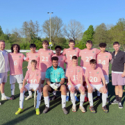 Eine Fußballmannschaft mit rosa Trikots steht für ein Gruppenfoto auf einem Sportplatz.