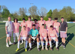 Eine Fußballmannschaft mit rosa Trikots steht für ein Gruppenfoto auf einem Sportplatz.