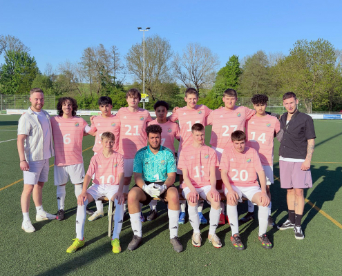 Eine Fußballmannschaft mit rosa Trikots steht für ein Gruppenfoto auf einem Sportplatz.