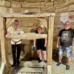 Drei Männer und eine Frau stehen vor einer historischen Seilwinde umgeben von Gesteinsmauern.