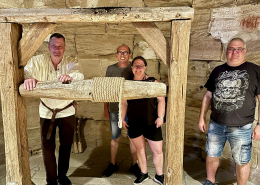 Drei Männer und eine Frau stehen vor einer historischen Seilwinde umgeben von Gesteinsmauern.