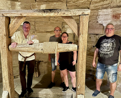 Drei Männer und eine Frau stehen vor einer historischen Seilwinde umgeben von Gesteinsmauern.