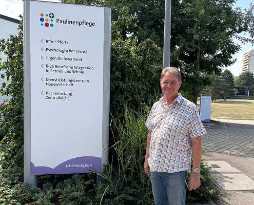 Ein Mann steht vor einem Paulinenpflege-Wegweiser des BBW Winnenden.