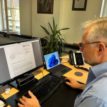 Ein Mann sitzt an einem Schreibtisch und schaut in seinen Computer-Bildschirm. Darauf ist der Offene Brief zu sehen.