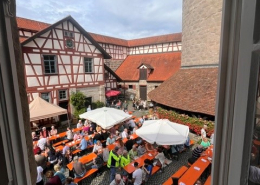Blick aus dem Fenster auf Menschen, die auf Bierbänken sitzen.