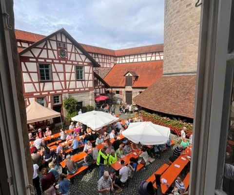 Blick aus dem Fenster auf Menschen, die auf Bierbänken sitzen.