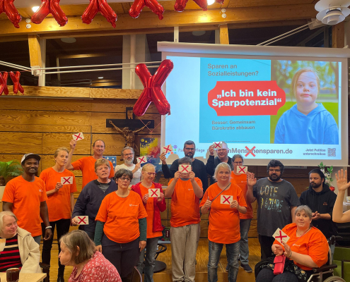 Der Bewohnerbeirat der Paulinenpflege steht auf der Bühne. Die Personen halten Postkarten mit "Nicht am Menschen sparen" in die Kamera.